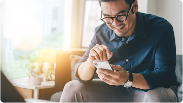 A man using a smartphone while sitting on a couch and smiling.